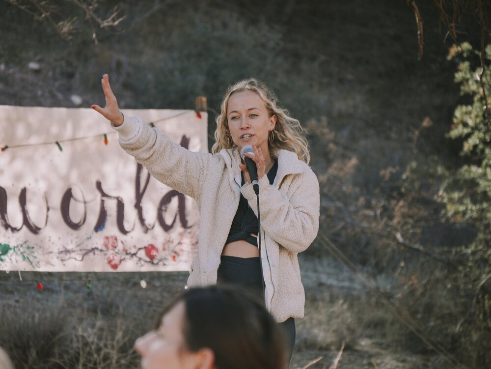 Skylar speaking on stage with a projection screen and sound bowls